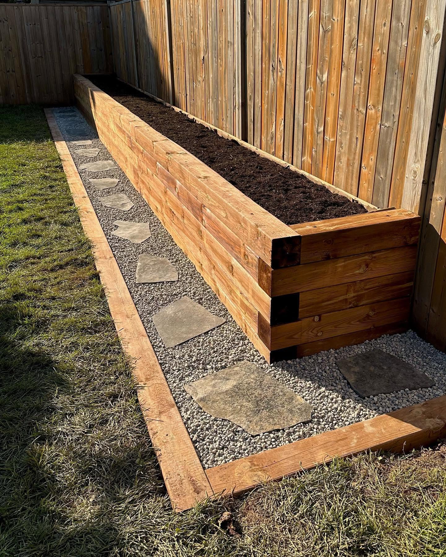 Wood raised garden bed filled with soil beside a gravel path with flagstone steps